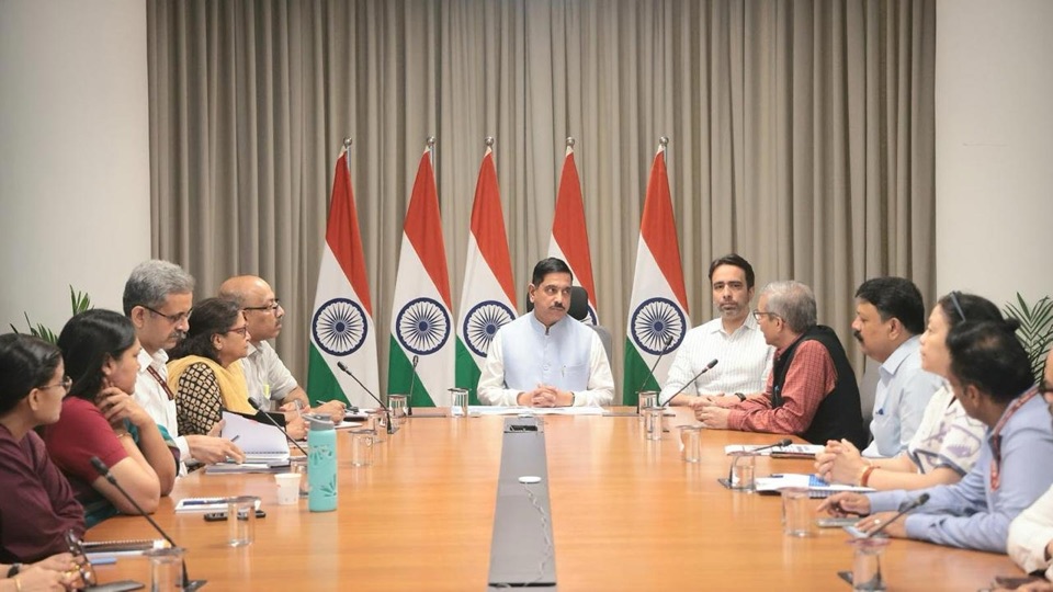Pralhad Joshi at the head of a long conference table with officials seated on both sides and Indian flags behind