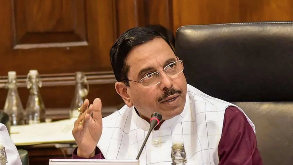 Pralhad Joshi gesturing while speaking into a table microphone at a meeting