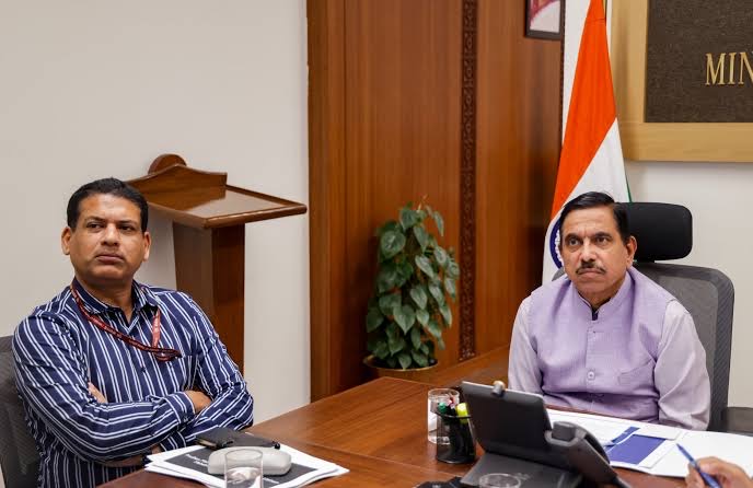 Pralhad Joshi seated at a desk beside an official, both looking towards a screen