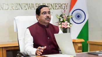Pralhad Joshi seated at a desk with papers, the words Renewable Energy on the wall behind him and the Indian flag to the side
