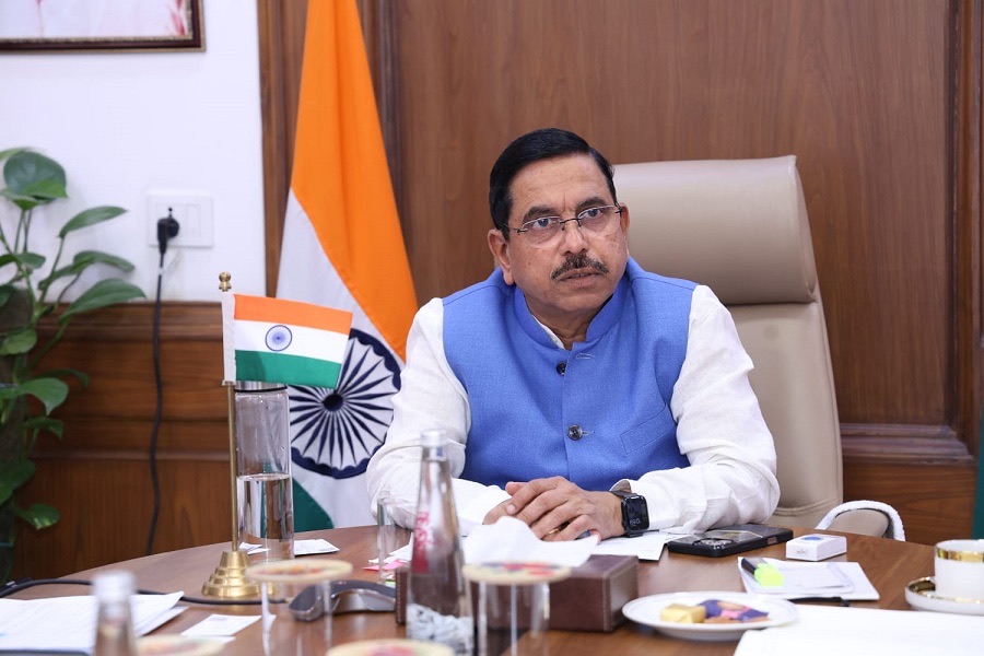 Pralhad Joshi seated at a desk with the Indian flag behind and a small desk flag in front
