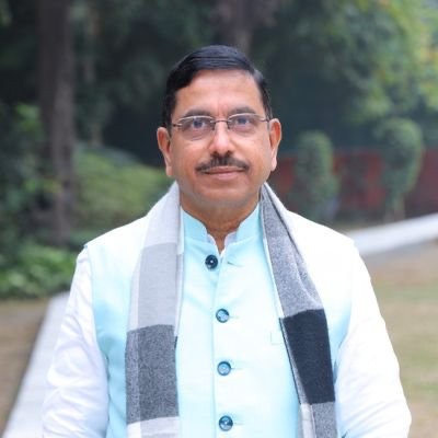 Portrait of Pralhad Joshi outdoors in a garden, wearing a light blue kurta and a grey scarf