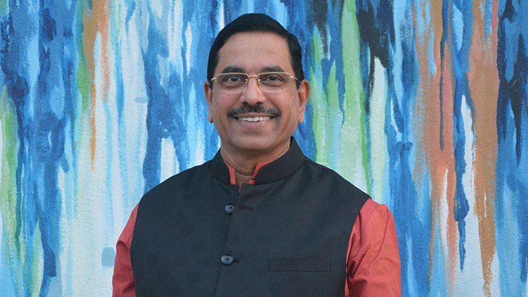 Smiling portrait of Pralhad Joshi in a black waistcoat in front of a colourful painted wall