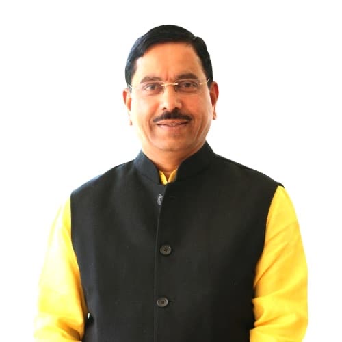Portrait of Pralhad Joshi in a black waistcoat over a yellow kurta against a white background