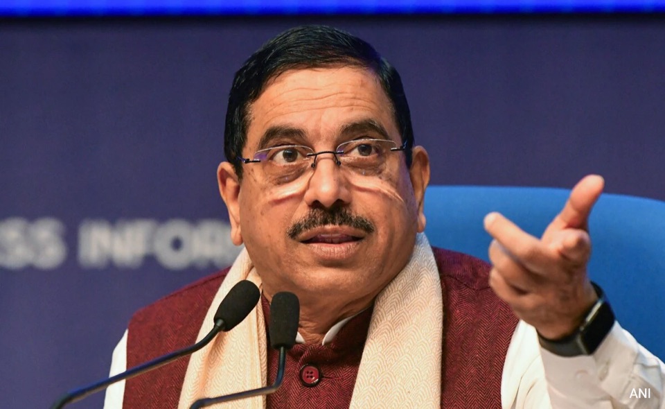 Pralhad Joshi gesturing while addressing a press conference at a table with microphones