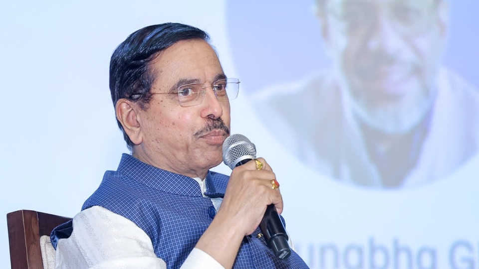 Pralhad Joshi seated and speaking into a handheld microphone at a forum