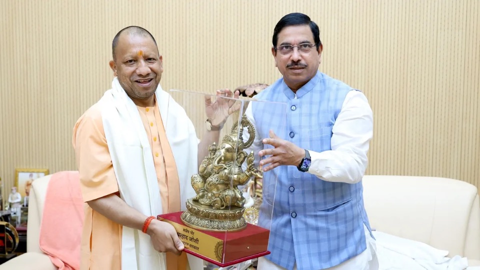 Pralhad Joshi and Uttar Pradesh Chief Minister Yogi Adityanath standing together holding a memento in a glass case
